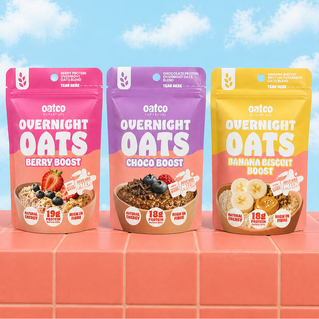 Three packages of Oatco Overnight Oats on a coral surface with a blue sky background